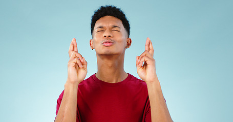 Image showing Man, eyes closed and fingers crossed for hope in studio in mock up for giveaway, win or luck. Young, male model and Cape Town on blue background by announcement, alert or promotion in space for prize