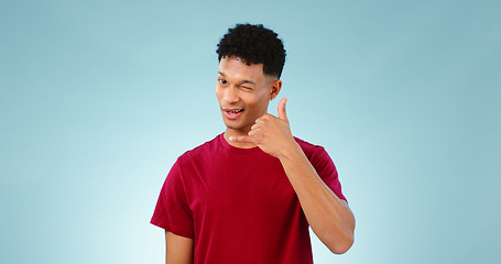 Image showing Portrait, man and wink to call me in studio on blue background in communication mockup. Cape Town, male model and flirting with hand emoji for connection, cellular or network with contact in space
