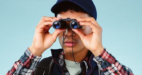 Image showing Binocular, hiking and man travel, search or adventure and explore isolated on a blue background. Young person trekking, lens vision and sightseeing or birdwatching gear for safari holiday in studio