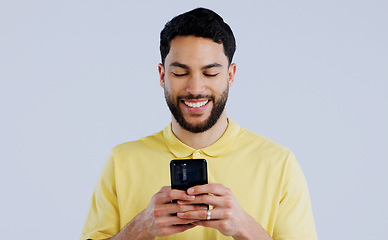 Image showing Man, smile and typing with phone in studio, scroll social media and reading notification on white background. Happy indian model download app, mobile games or search contact information on smartphone