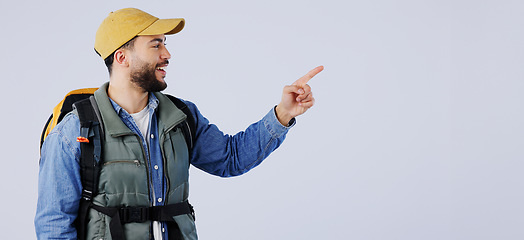 Image showing Happy man, backpack and pointing on mockup for hiking, adventure or travel tips against a studio background. Male person, model or hiker smile with bag showing trekking list, deal or advertising