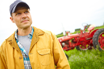 Image showing Thinking aboyt ways to improve the farm. A farmer standing in a field with a tractor parked behind him - Copyspace.