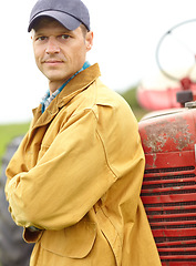 Image showing I help provide your fruit and veg - Farmer. Portrait of a farmer with his arms crossed while leaning against the hood of his tractor.