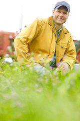 Image showing Hes a happy and confident farmer. Portrait of a farmer kneeling in a field with his tractor parked behind him.