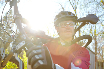 Image showing Deciding which way to go next...Closeup of a male cyclist wearing glasses, a helmet and gloves while carrying his bicycle through the woods. Mature sportsman out cycling in nature on a sunny day.