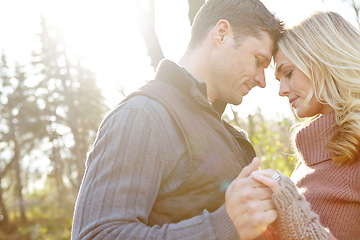 Image showing Loving young couple being affectionate while sharing a romantic moment in the woods. Married man and woman touching heads and holding hands while standing together in nature in Autumn