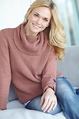 Image showing Portrait of a beautiful blonde woman relaxing at home on the sofa in the lounge. Cheerful female sitting on the couch in the living room alone on the weekend. Comfy, smiling and resting inside