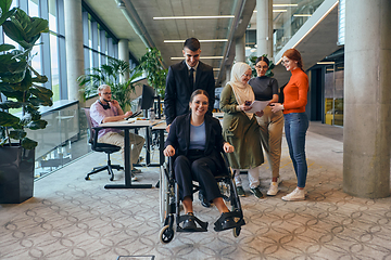 Image showing A diverse group of business colleagues is having fun with their wheelchair-using colleague, demonstrating their attention and inclusivity in the workplace