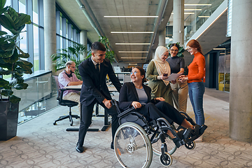 Image showing A diverse group of business colleagues is having fun with their wheelchair-using colleague, demonstrating their attention and inclusivity in the workplace
