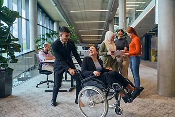 Image showing A diverse group of business colleagues is having fun with their wheelchair-using colleague, demonstrating their attention and inclusivity in the workplace