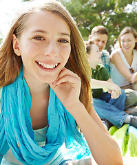 Image showing She loves summer time with her family. A pretty young girl sitting outdoors in the park with her family in the background.