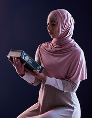 Image showing Quran, faith and muslim woman reading in a studio with traditional clothes and hijab. Serious, religion and young islamic female person studying the holy Arabic book isolated by a black background.