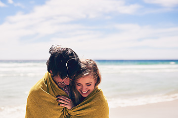 Image showing Escaping the cold ocean breeze. an affectionate young couple wrapped in a blanket on the beach.