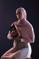 Image showing Quran, religion and portrait of a muslim woman in a studio with traditional clothes and hijab. Serious, faith and young islamic female person with the holy Arabic book isolated by a black background.