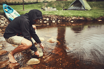 Image showing Nature has everything you need. a young man filling water from a lake into a pot at a campsite.