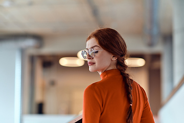 Image showing In a vibrant modern startup office, a businesswoman with striking orange hair is immersed in her work at her desk, embodying the dynamic and creative spirit of contemporary entrepreneurship.