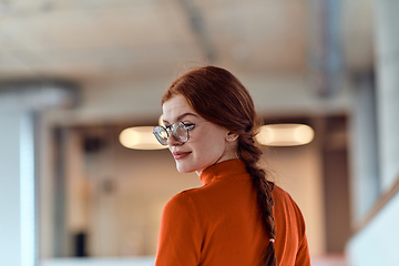 Image showing In a vibrant modern startup office, a businesswoman with striking orange hair is immersed in her work at her desk, embodying the dynamic and creative spirit of contemporary entrepreneurship.