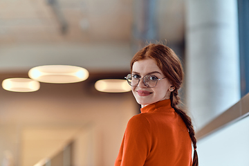 Image showing In a vibrant modern startup office, a businesswoman with striking orange hair is immersed in her work at her desk, embodying the dynamic and creative spirit of contemporary entrepreneurship.