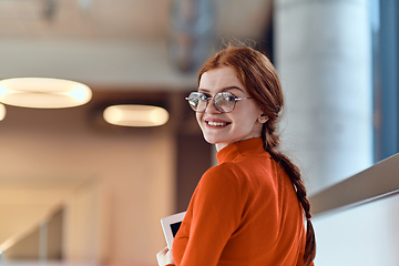 Image showing In a vibrant modern startup office, a businesswoman with striking orange hair is immersed in her work at her desk, embodying the dynamic and creative spirit of contemporary entrepreneurship.