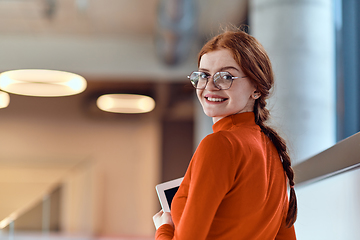 Image showing In a vibrant modern startup office, a businesswoman with striking orange hair is immersed in her work at her desk, embodying the dynamic and creative spirit of contemporary entrepreneurship.