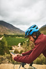 Image showing Technology takes him places. a young man using his cellphone while cycling along a trail.