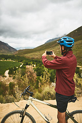 Image showing Its a great ride made even better by breathtaking views. a young man taking a photo while cycling along a trail.