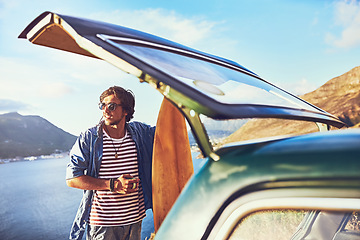 Image showing Where will the road lead me next. a happy young man standing outside his car during a roadtrip.