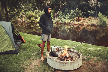 Image showing Theres so much to appreciate in the great outdoors. a young man looking thoughtful while preparing food at a campsite fire.