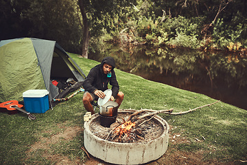 Image showing Cooking over the campfire. a young man preparing food at a campsite fire.
