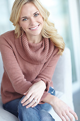 Image showing Portrait of a young blonde woman relaxing at home on the sofa in the lounge. Cheerful female sitting on the couch in the living room alone on the weekend. Comfy, smiling and resting inside