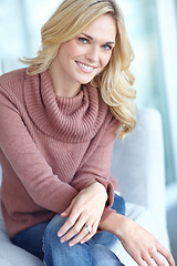 Image showing Portrait of a beautiful blonde woman relaxing at home on the sofa in the lounge. Cheerful female sitting on the couch in the living room alone on the weekend. Comfy, smiling and resting inside