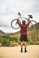 Image showing The best adventures are enjoyed on a bike. Rearview shot of a young man standing with his bike raised in victory outside.