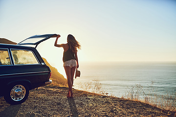 Image showing Happiness is a journey, not a destination. Rearview shot of a young woman standing next to her car during a roadtrip.