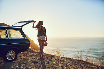 Image showing Its a view worth driving for. Rearview shot of a young woman standing next to her car during a roadtrip.