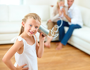 Image showing She loves compliments. A little girl listening through a tin can connected to her parents in the background.