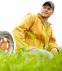 Image showing He is at home on the farm. A farmer kneeling in a field with his tractor parked behind him.