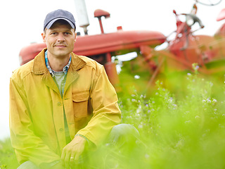 Image showing Enjoying the feeling of spring. Portrait of a farmer kneeling in a field with his tractor parked behind him.