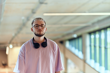 Image showing In a contemporary startup office, a modern blond entrepreneur stands, engrossed in his smartphone, epitomizing the dynamic and tech-savvy essence of the modern business world.