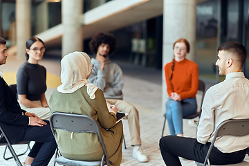 Image showing A diverse group of young business entrepreneurs gathered in a circle for a meeting, discussing corporate challenges and innovative solutions within the modern confines of a large corporation