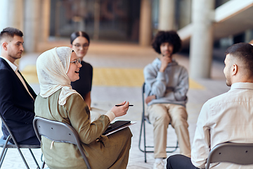 Image showing A diverse group of young business entrepreneurs gathered in a circle for a meeting, discussing corporate challenges and innovative solutions within the modern confines of a large corporation