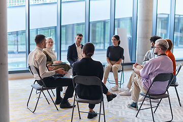 Image showing A diverse group of young business entrepreneurs gathered in a circle for a meeting, discussing corporate challenges and innovative solutions within the modern confines of a large corporation