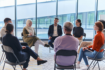 Image showing A diverse group of young business entrepreneurs gathered in a circle for a meeting, discussing corporate challenges and innovative solutions within the modern confines of a large corporation