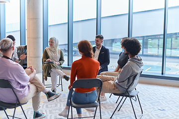 Image showing A diverse group of young business entrepreneurs gathered in a circle for a meeting, discussing corporate challenges and innovative solutions within the modern confines of a large corporation