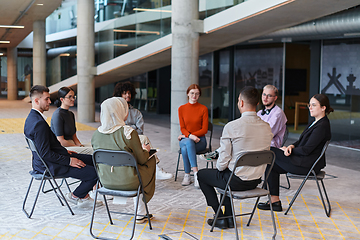 Image showing A diverse group of young business entrepreneurs gathered in a circle for a meeting, discussing corporate challenges and innovative solutions within the modern confines of a large corporation