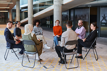 Image showing A diverse group of young business entrepreneurs gathered in a circle for a meeting, discussing corporate challenges and innovative solutions within the modern confines of a large corporation