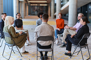 Image showing A diverse group of young business entrepreneurs gathered in a circle for a meeting, discussing corporate challenges and innovative solutions within the modern confines of a large corporation