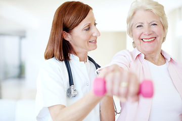 Image showing The strength of her resolve - Senior Care. Smiling elderly female is assisted by her nurse as she lifts a dumbbell - Focus on background.