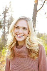 Image showing Headshot of a beautiful blonde woman standing in a park in fall. Happy attractive young female smiling outside on an autumn day in nature. Relaxing lady with perfect teeth showing laugh lines