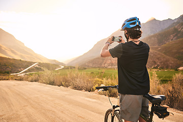 Image showing Capturing the beauty along the trail. a young man taking a photo while cycling along a trail.