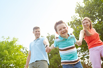 Image showing Pulling mom and dad along. Low angle portrait of a happy boy walking hand in hand with his parents.